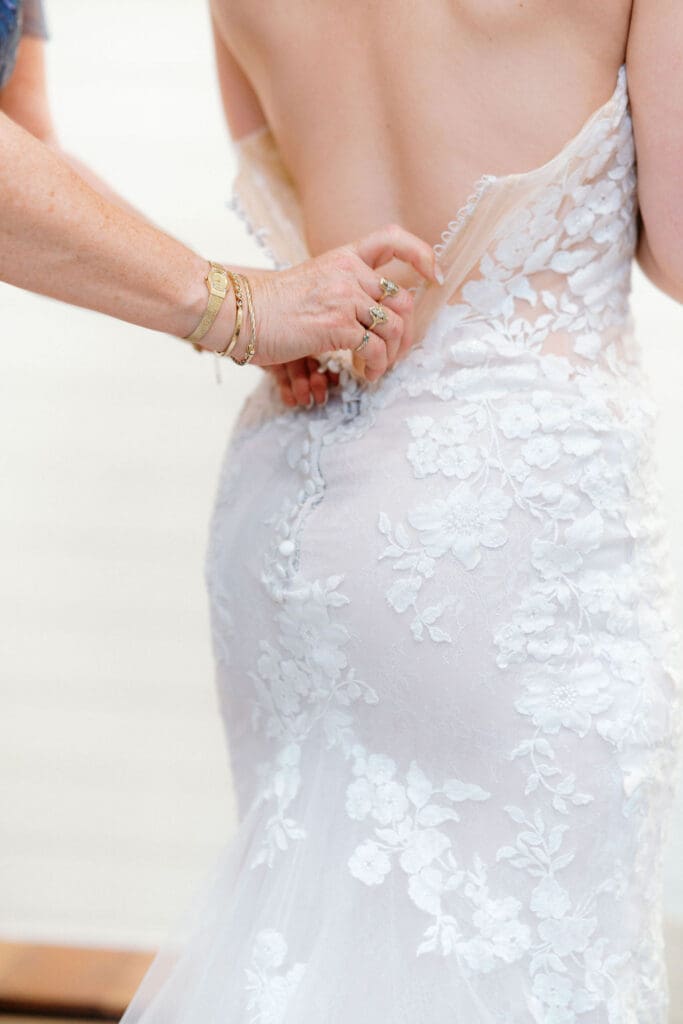 Bride putting on lace wedding dress in bridal suite at Harper’s Vineyard.