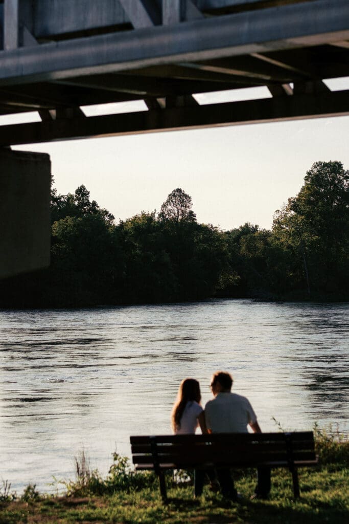 Couple sitting on bench by water at Seven Islands during their Knoxville engagement session