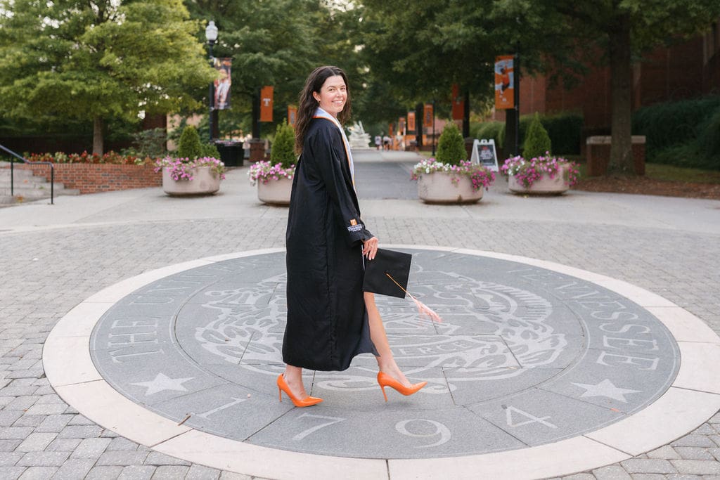girl wearing orange heels and a cap and gown walks in knoxville tennessee for UTK senior photos