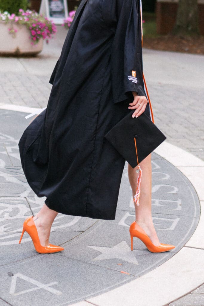 girl wearing orange heels and a cap and gown walks in knoxville tennessee for UTK senior photos