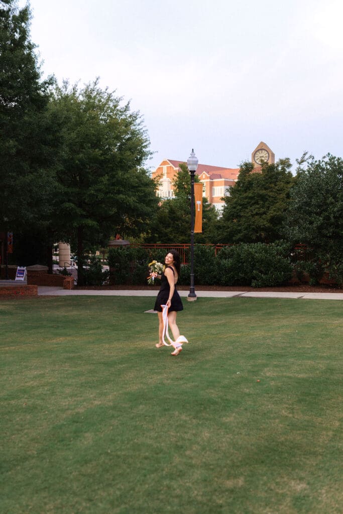 girl in black dress holds flowers and runs on hss lawn at the university of tennessee knoxville for senior photos