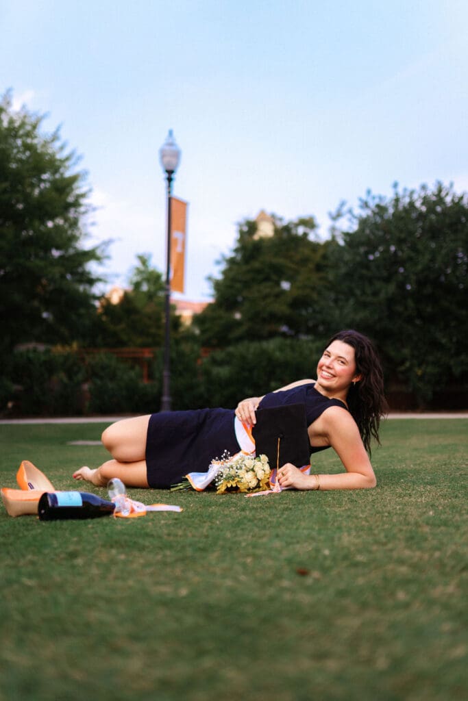 girl in black dress sits on HSS lawn with flowers and champagne at the university of tennessee knoxville