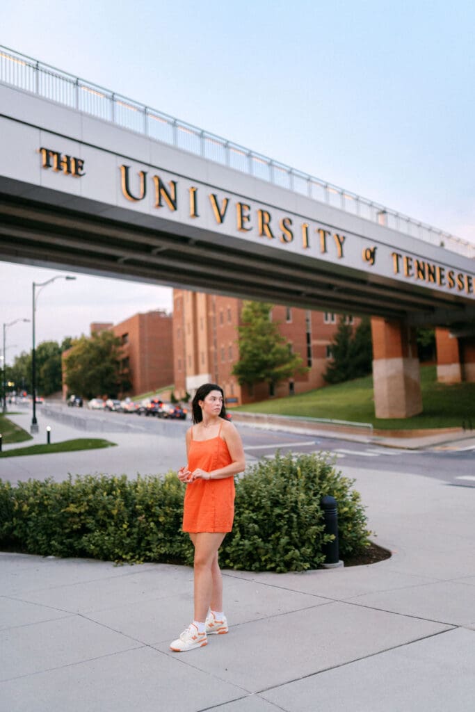 girl in orange dress stands in front of the university of tennessee bridge in knoxville tennessee