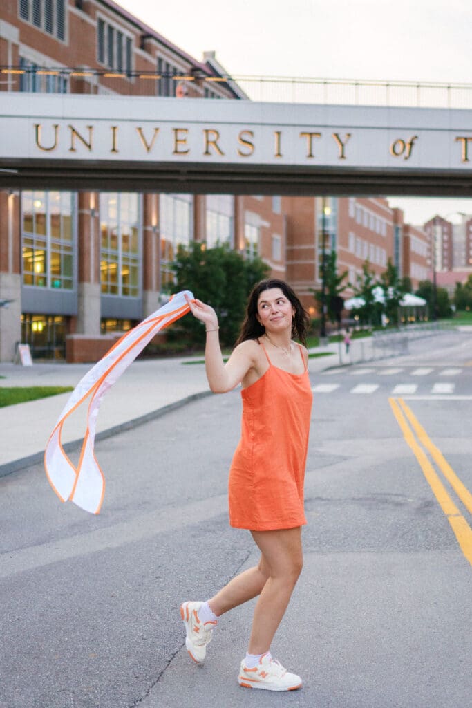 girl in orange dress and white sneakers runs in front of university of tennessee bridge in knoxville tennessee