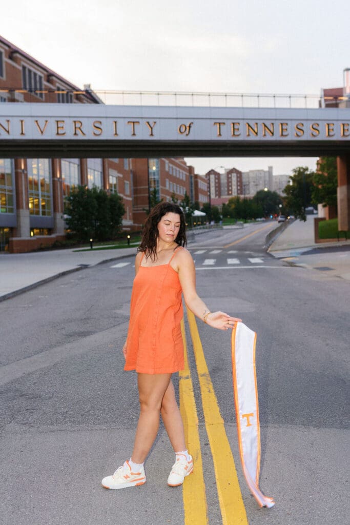 girl in orange dress poses with stole in front of the university of tennessee bridge in knoxville tennessee