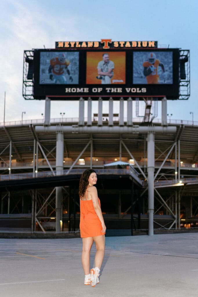 girl in orange dress and white sneakers on g10 garage in front of neyland stadium sign at utk campus