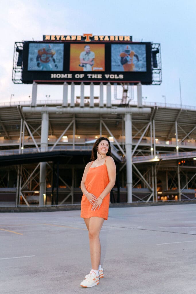 girl in orange dress and white sneakers on g10 garage in front of neyland stadium sign at university of tennessee campus