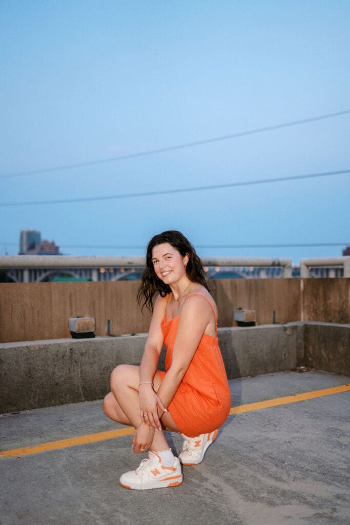 Grad in orange dress and white sneakers sits on top of g10 garage at the university of tennessee knoxville