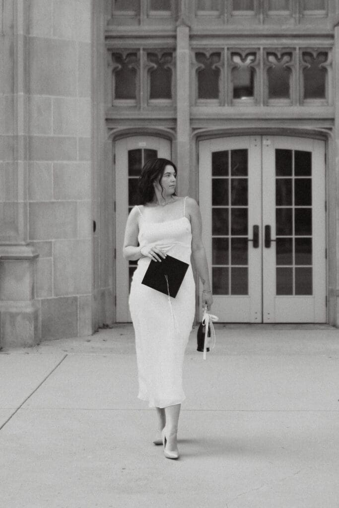 Rachel poses holding a cap in a white dress on the University of Tennessee Knoxville campus during her senior portrait session.