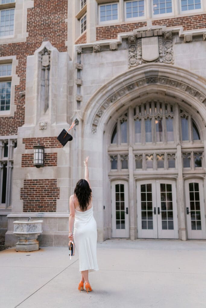 Rachel throws her cap in the air in a white dress on the University of Tennessee Knoxville campus during her senior portrait session.