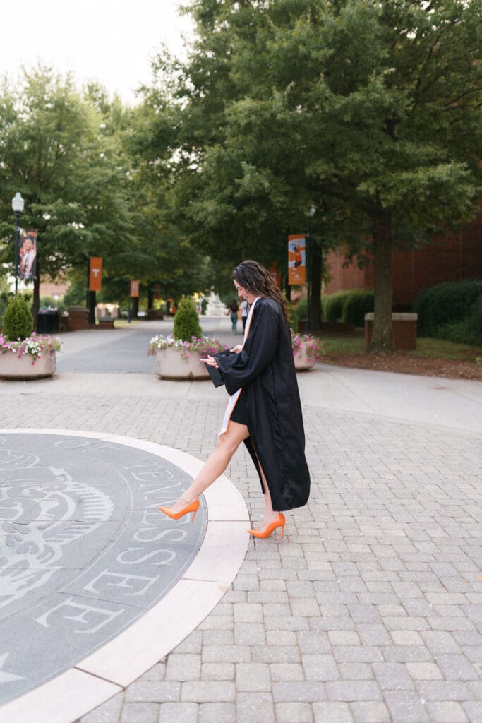 girl wearing orange heels and a cap and gown walks in knoxville tennessee for UTK senior photos