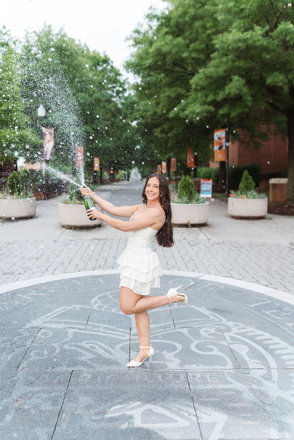 girl in white dress sprays champagne on the seal at the university of tennessee knoxville campus for senior photos