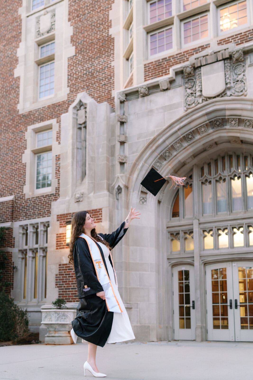 girl in graduation gown tosses cap in front of ayres hall on the university of tennessee campus in knoxville