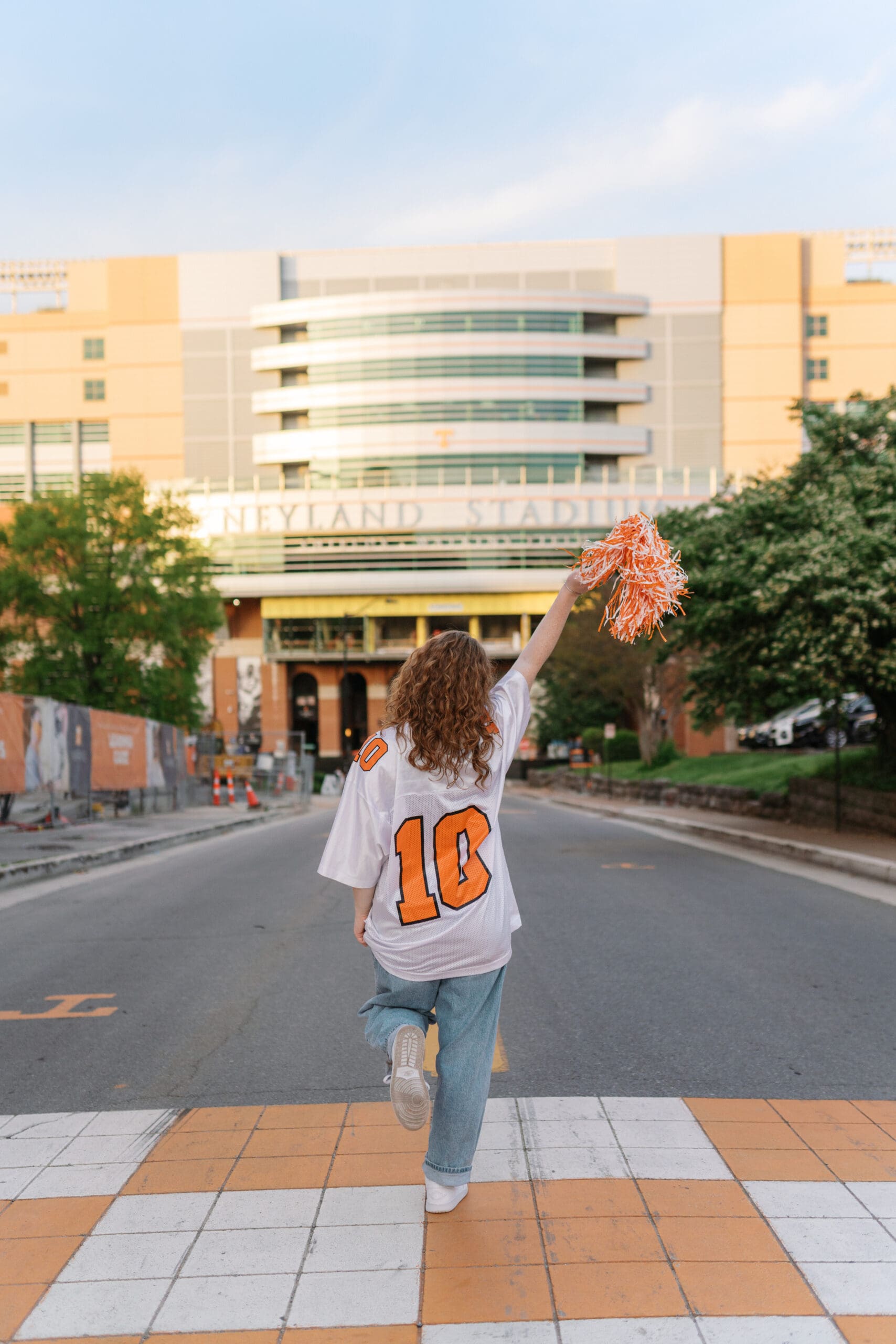 Girl in white volunteers jersey waves orange and white pom pom while standing in front of neyland stadium for grad pictures at the university of tennessee knoxville