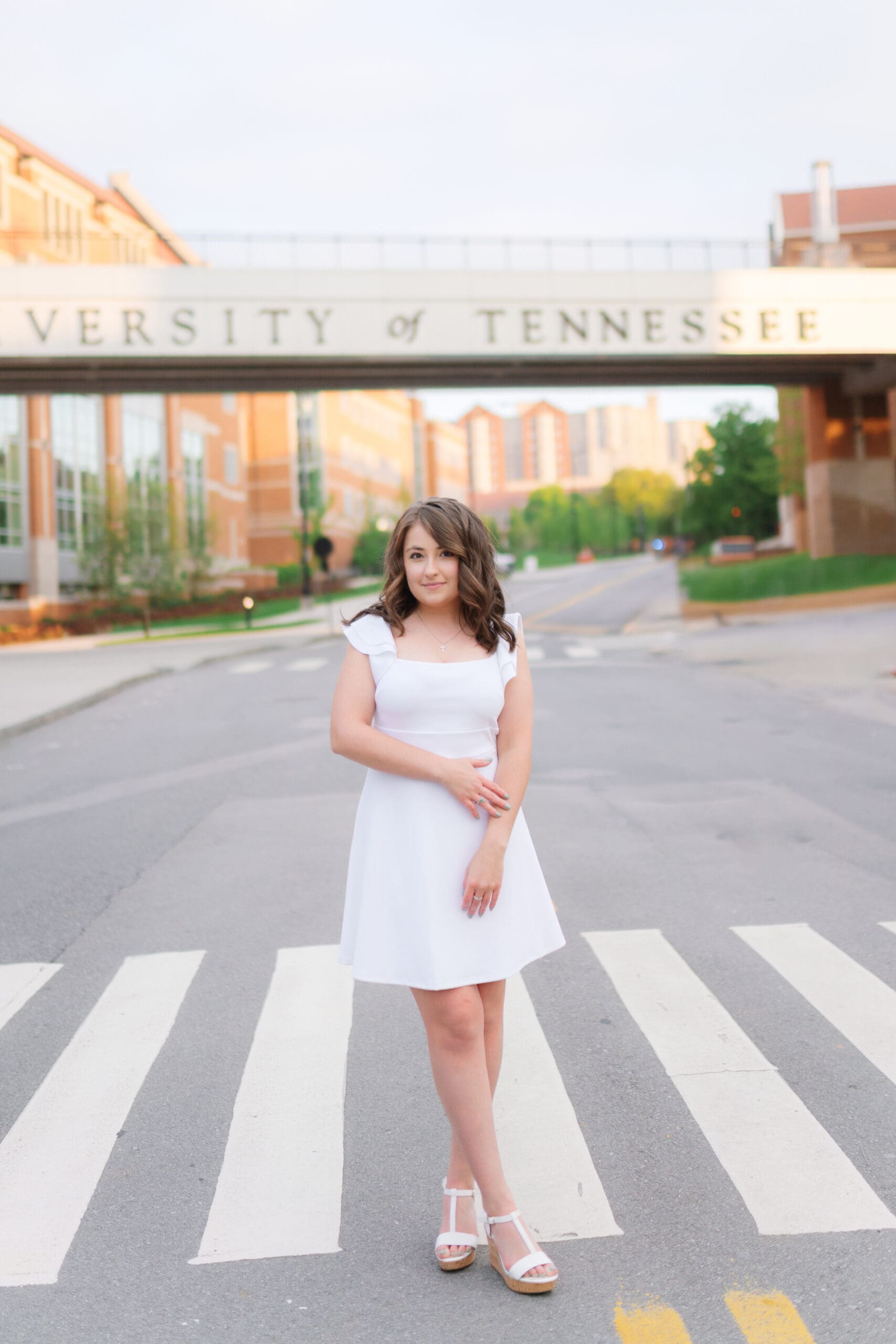 girl in white dress stands in front of the university of tennessee knoxville bridge for grad photos