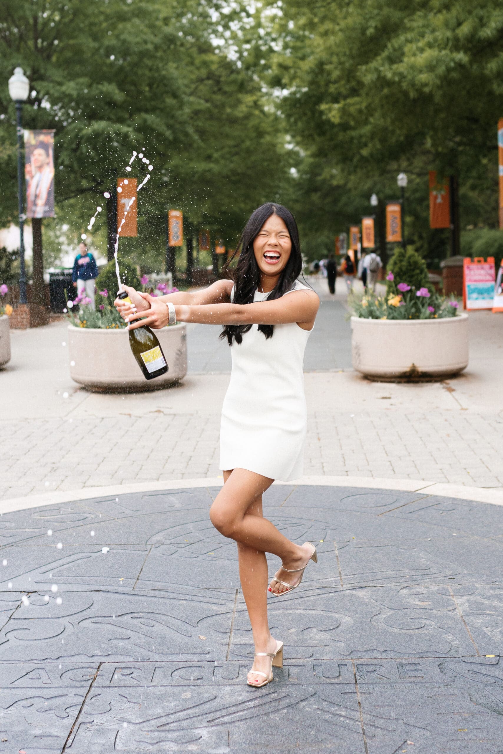 University of Tennessee senior wearing white dress sprays champagne during her UTK graduation photoshoot