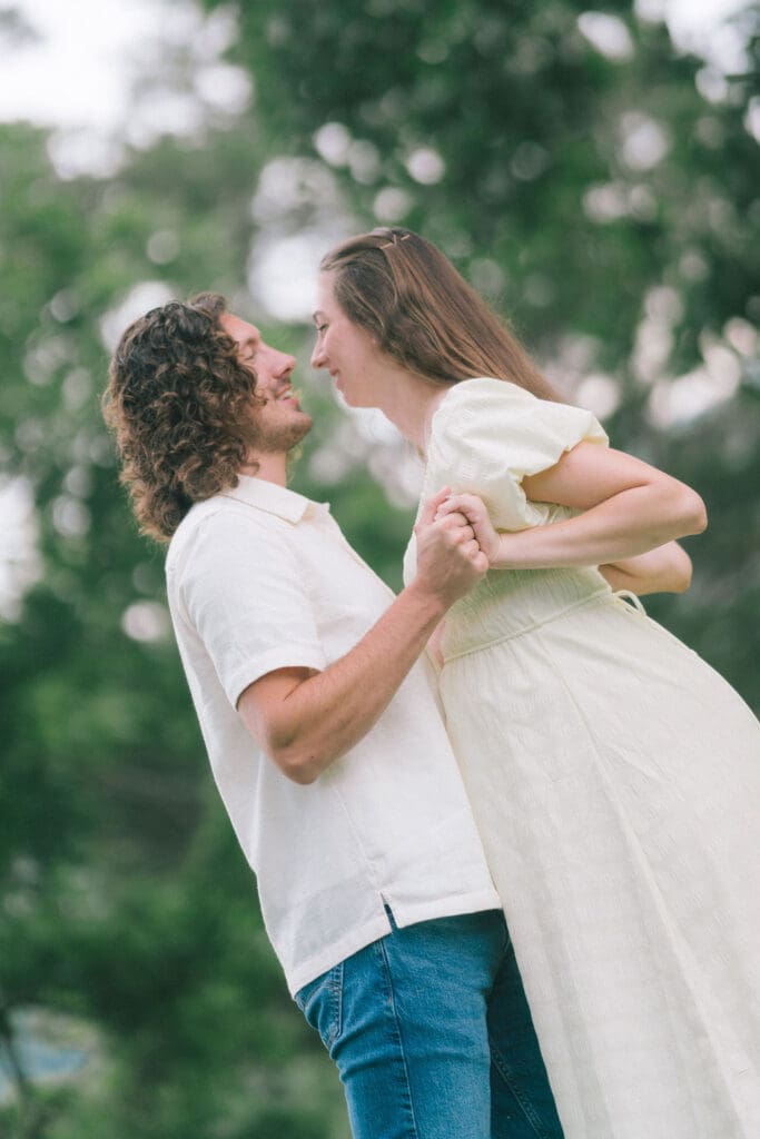 Expecting couple dancing holding hands under trees during maternity session at Cove Lake State Park, Tennessee