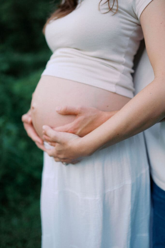 Detail shot of pregnant belly held with mom and dad hands, taken at Cove Lake in East Tennessee