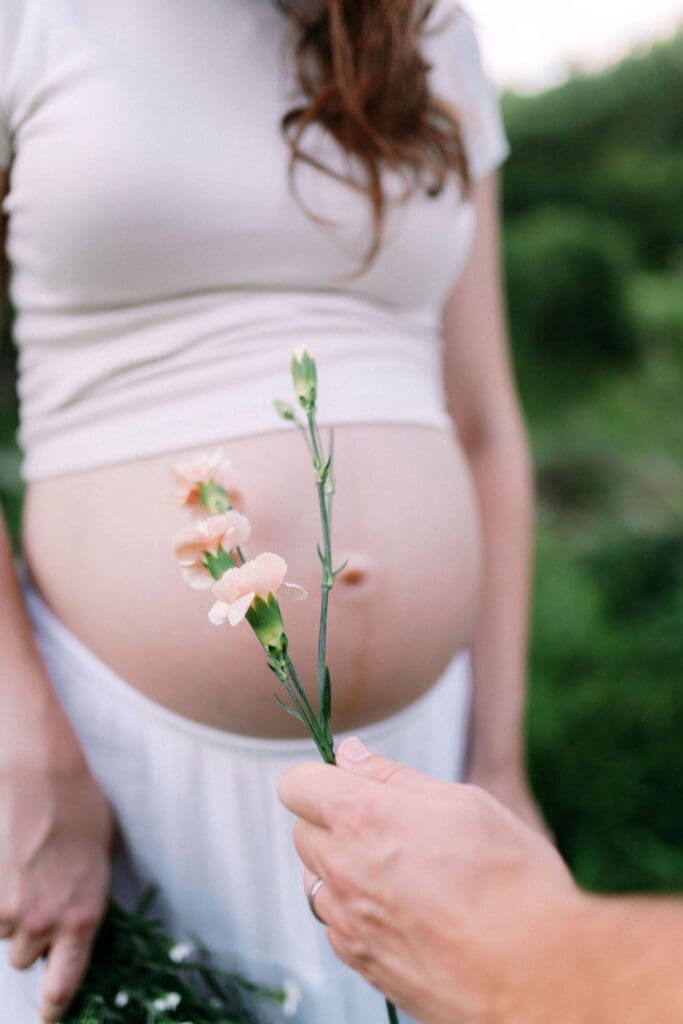 Detail shot of pregnant belly with flowers held in front, taken at Cove Lake in East Tennessee