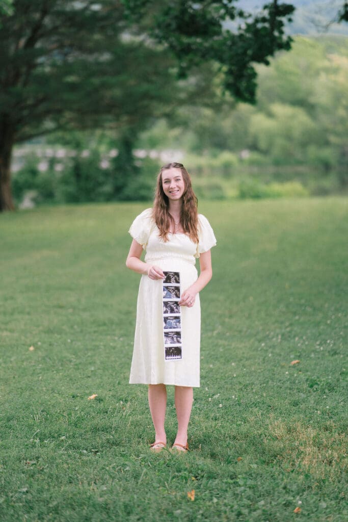 Expecting mother holds sonogram in field during maternity session at Cove Lake State Park near Knoxville, Tennessee