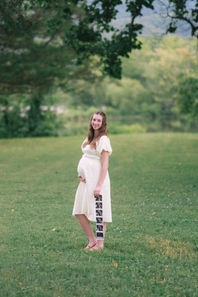 Expecting mother holds sonogram in field during maternity session at Cove Lake State Park near Knoxville, Tennessee