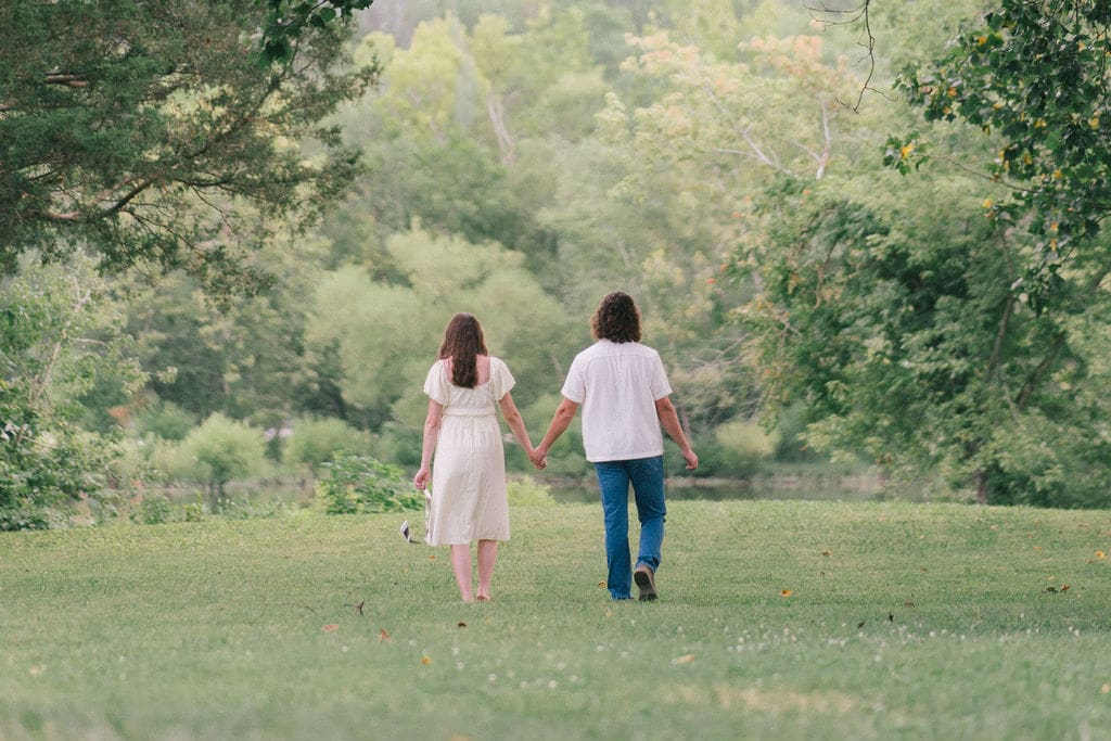 Couple holding hands walking through trees during maternity session at Cove Lake State Park, Tennessee