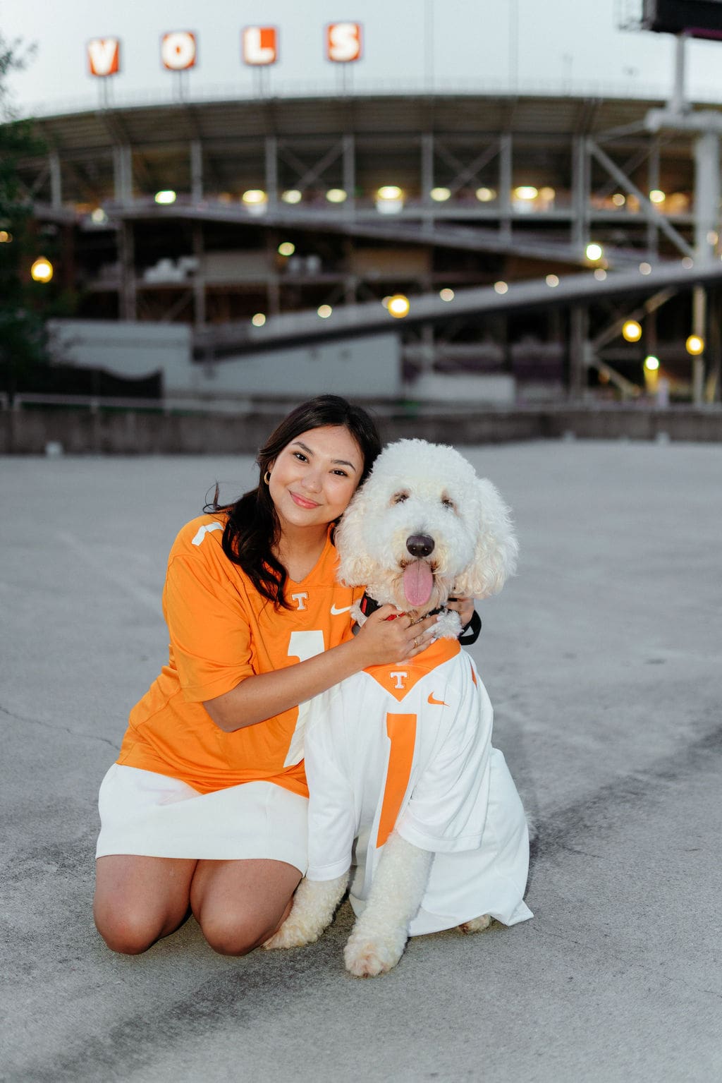 graduate in orange jersey smiles with doodle puppy at g10 garage by neyland stadium at the university of tennessee knoxville for UTK senior photos