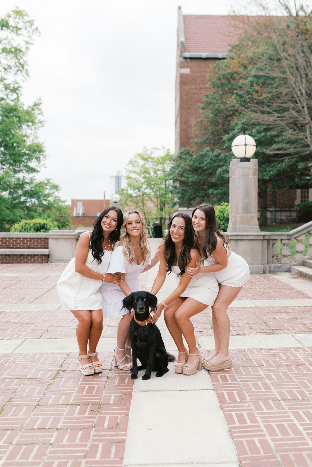 group of girls smile with dog at ayres hall on the university of tennessee knoxville campus during senior photos